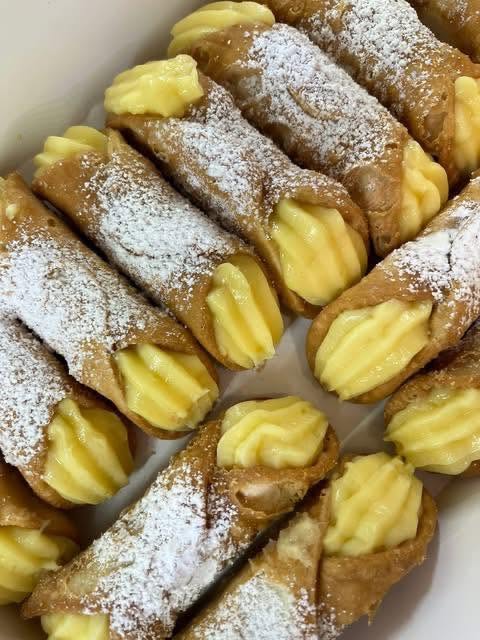Close-up of custard-filled cannoli dusted with icing sugar lined up on parchment paper