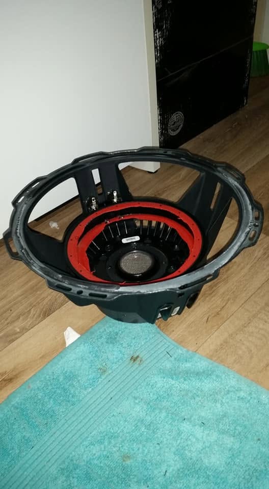 Black subwoofer basket with a red gasket ring sitting on a timber floor
