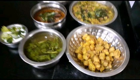 Multiple steel bowls of freshly prepared Indian dishes including sabzi, dal, and raita