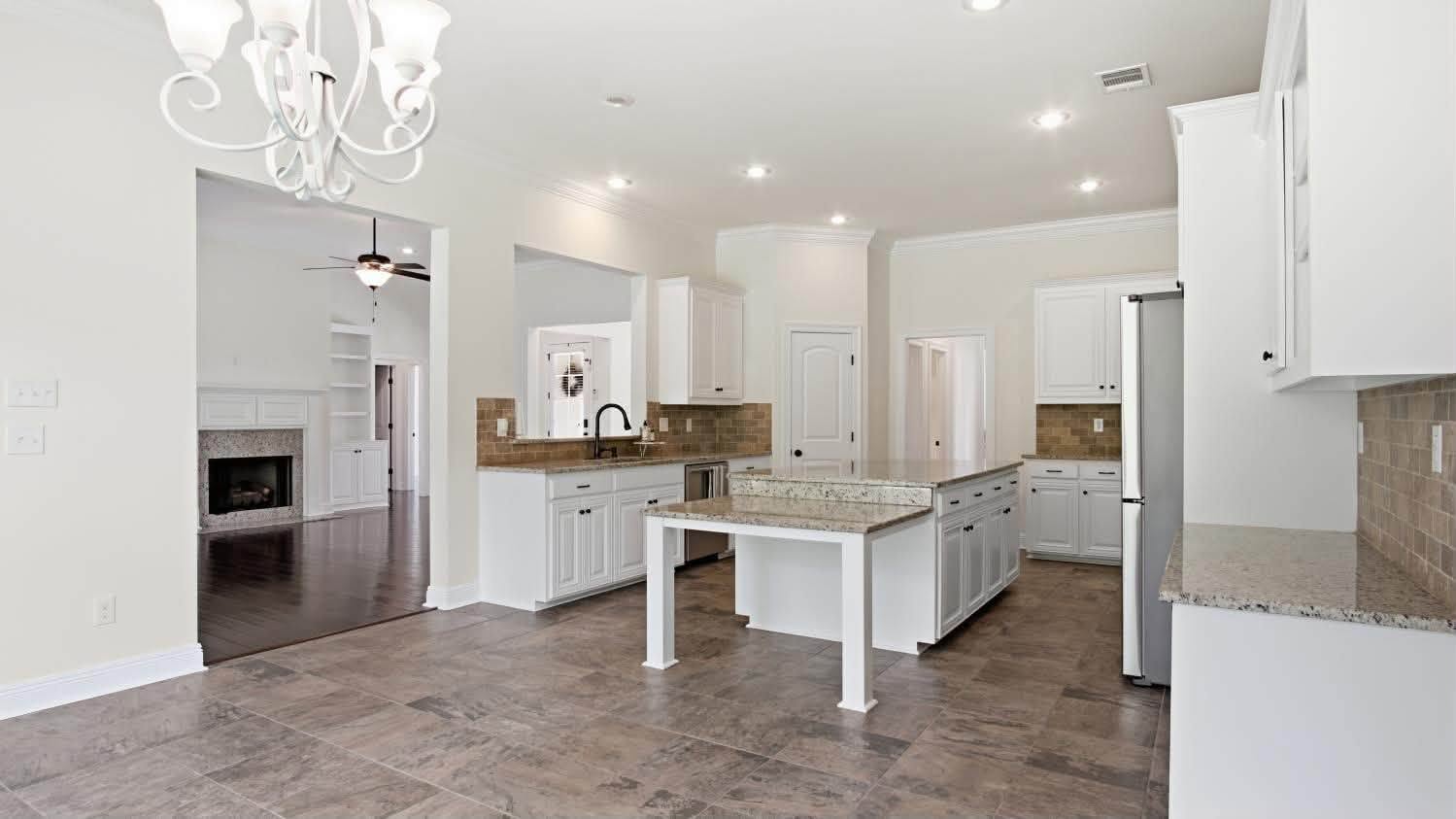 An open-plan kitchen with white cabinetry, granite benchtops and tiled flooring