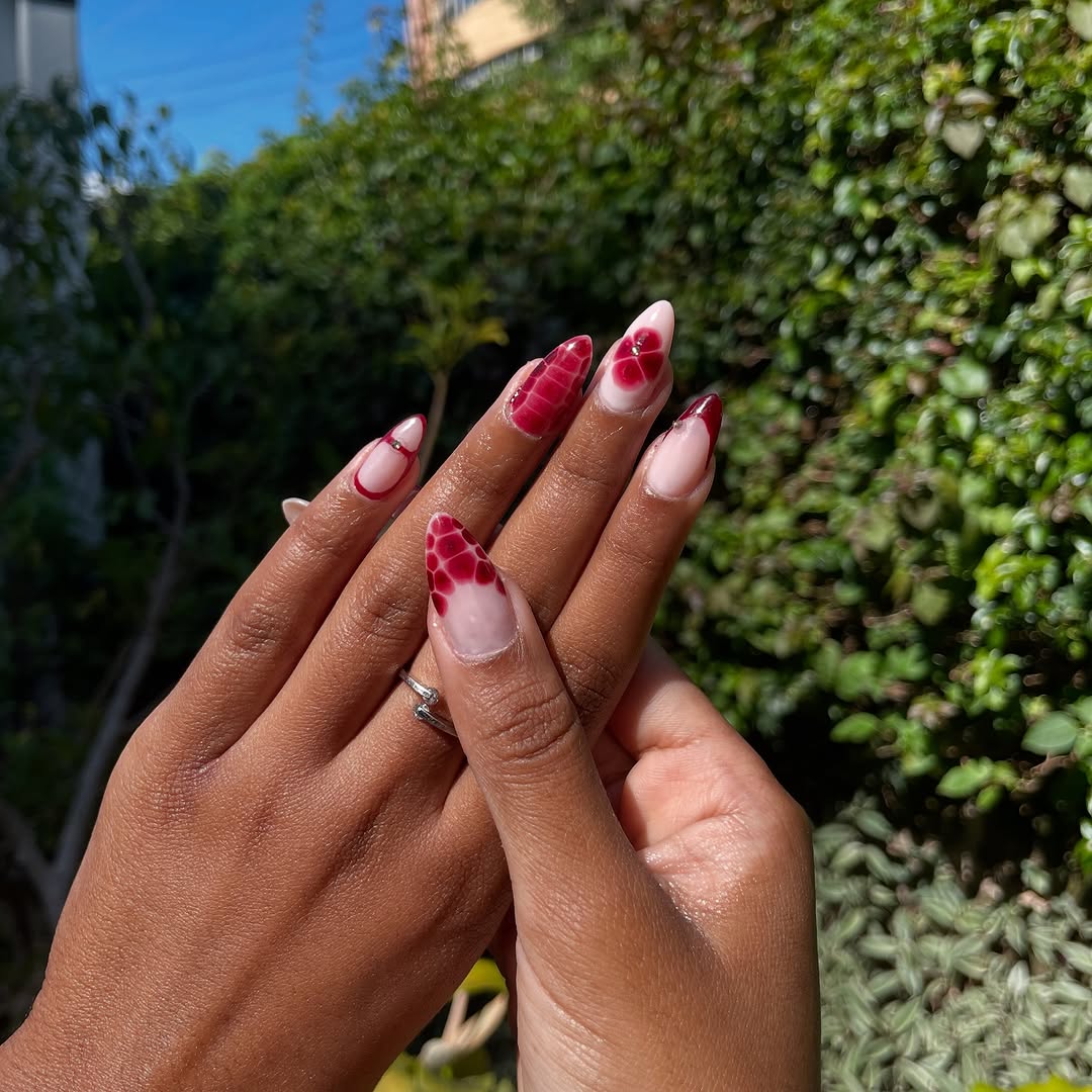 Red floral nail art on both hands against green foliage