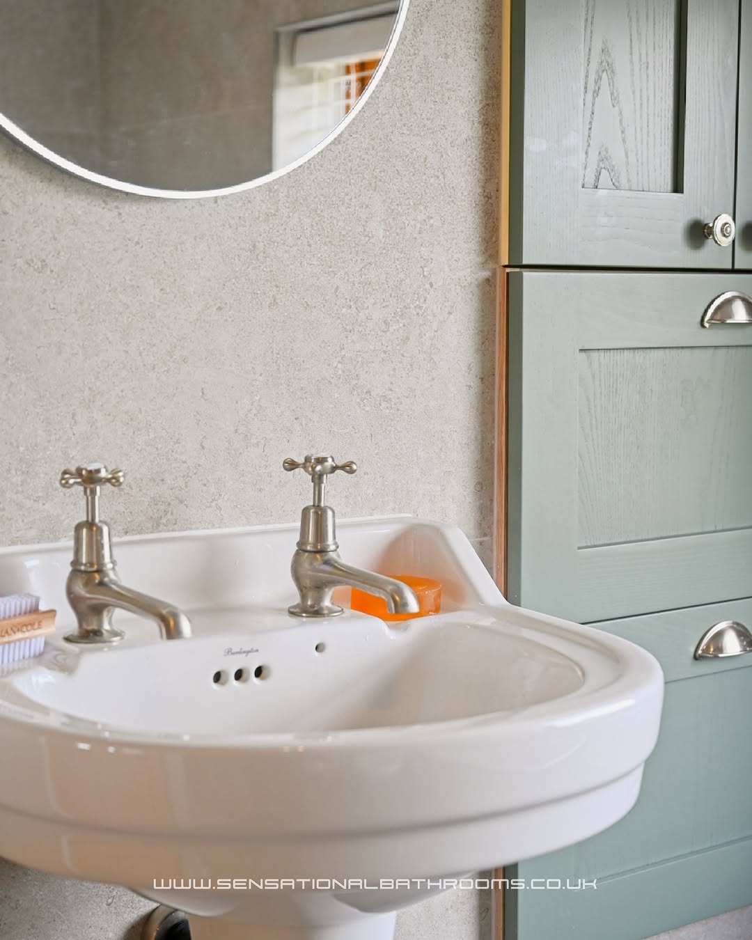 Classic pedestal basin with cross-handle brushed nickel taps and sage green storage cabinet