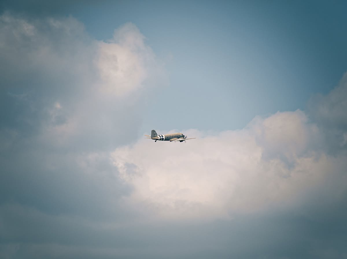 Colour photograph of a vintage aircraft flying against a blue-grey cloudy sky
