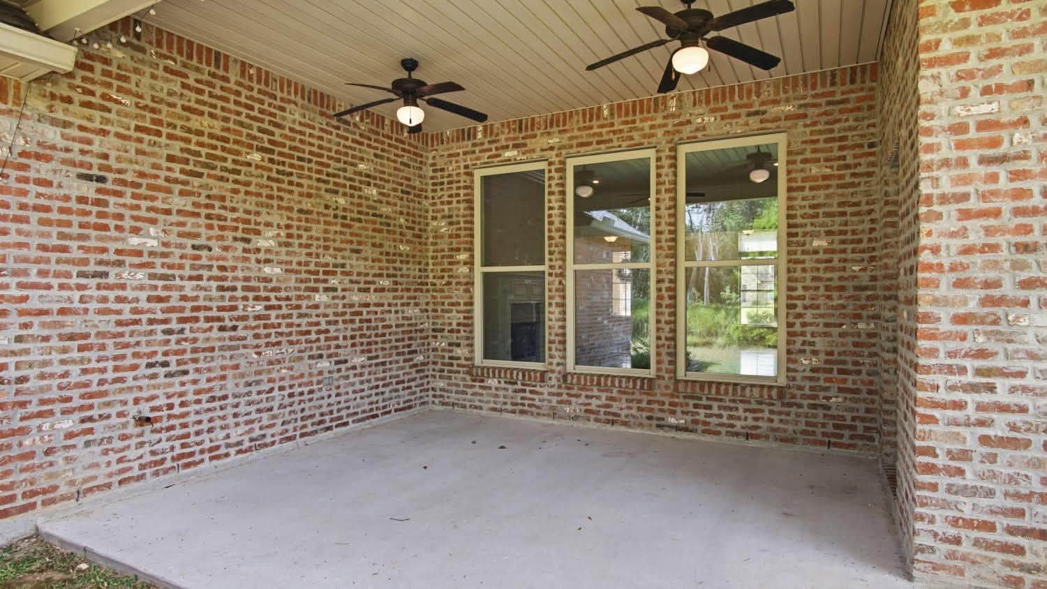A covered brick outdoor entertaining area with ceiling fans and large windows