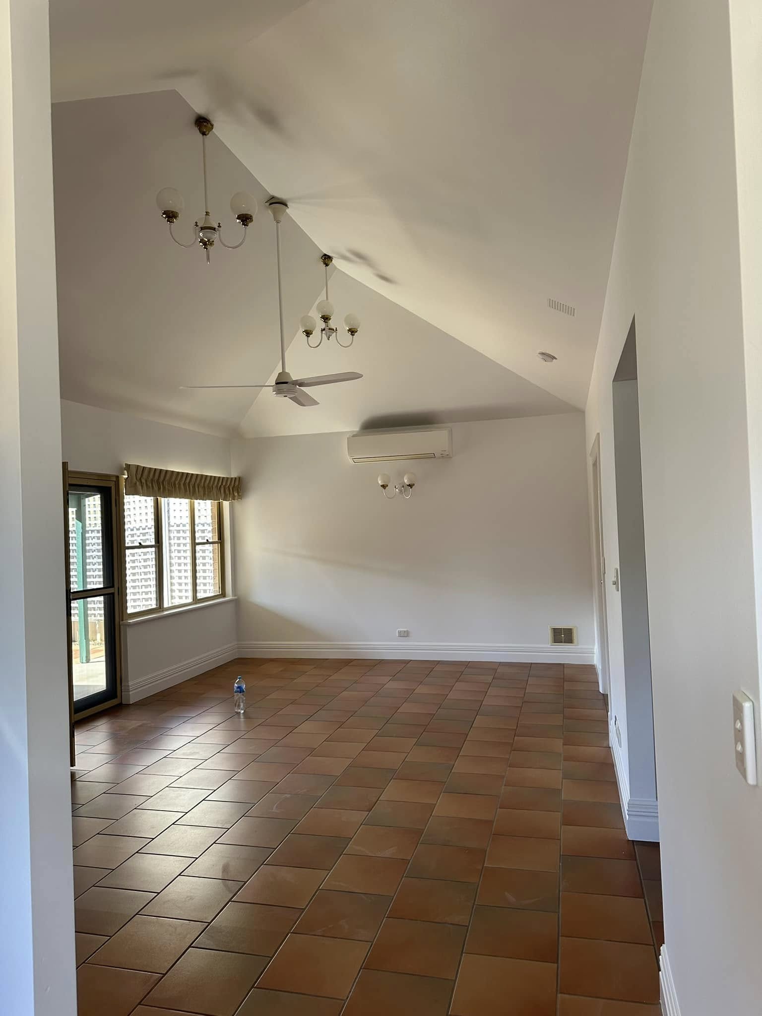 Large open vaulted-ceiling room with terracotta tiles and chandelier — freshly painted white walls