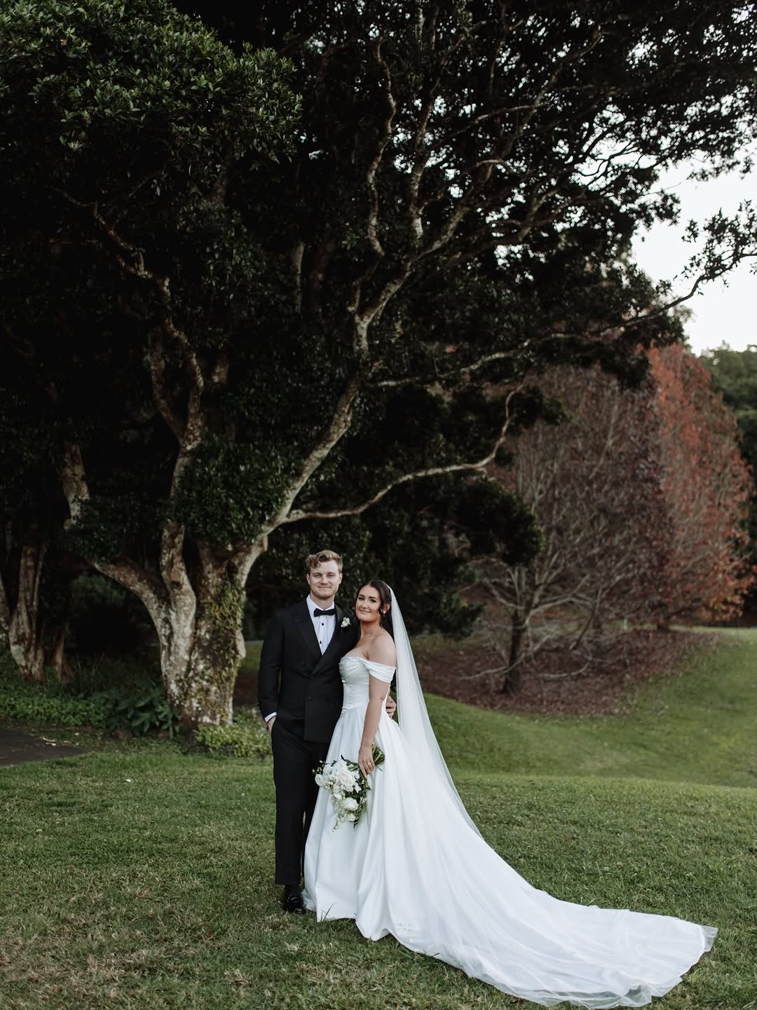 Wedding couple standing together in a lush garden with autumn-coloured trees in the background