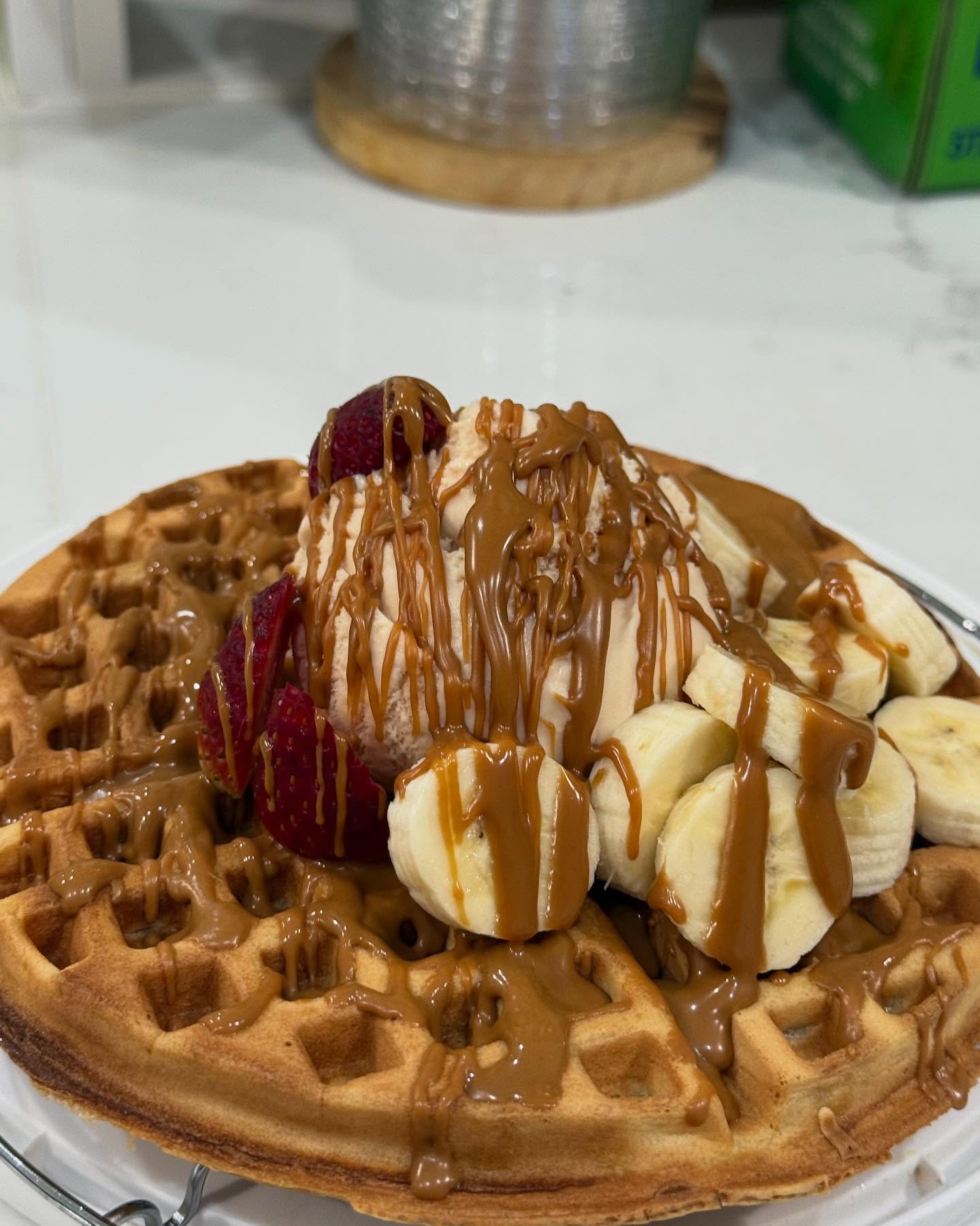 Waffle topped with ice cream, strawberries, banana slices and caramel drizzle