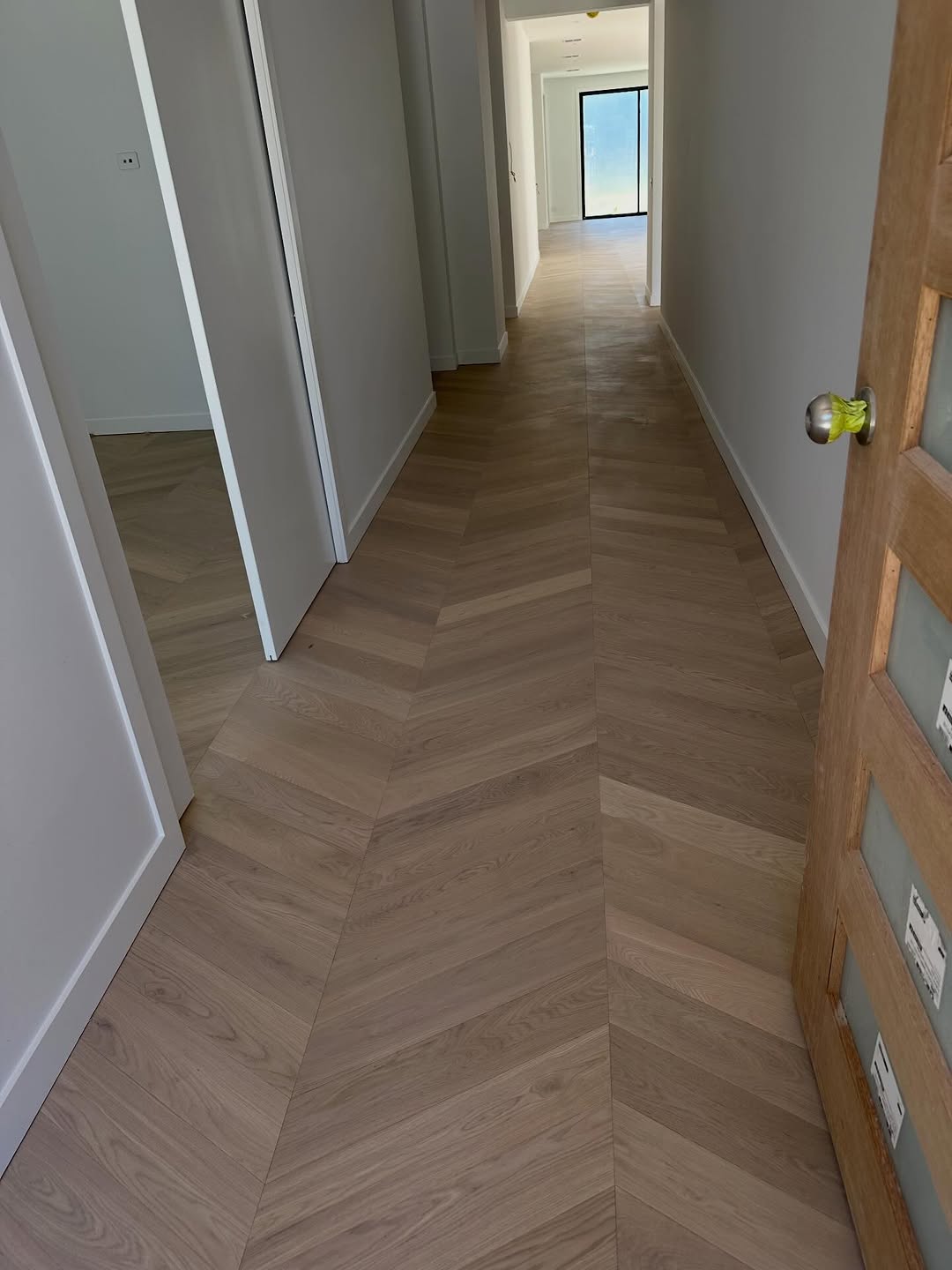 Chevron-pattern light oak timber flooring in a long new-build hallway