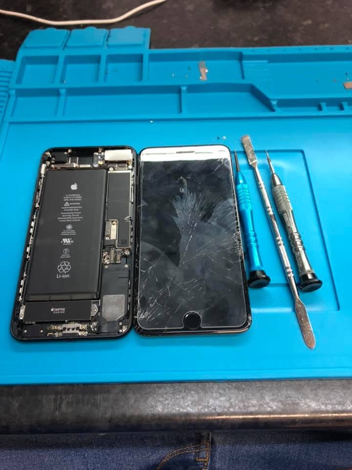 Technician's workbench showing an open iPhone being repaired with precision screwdrivers