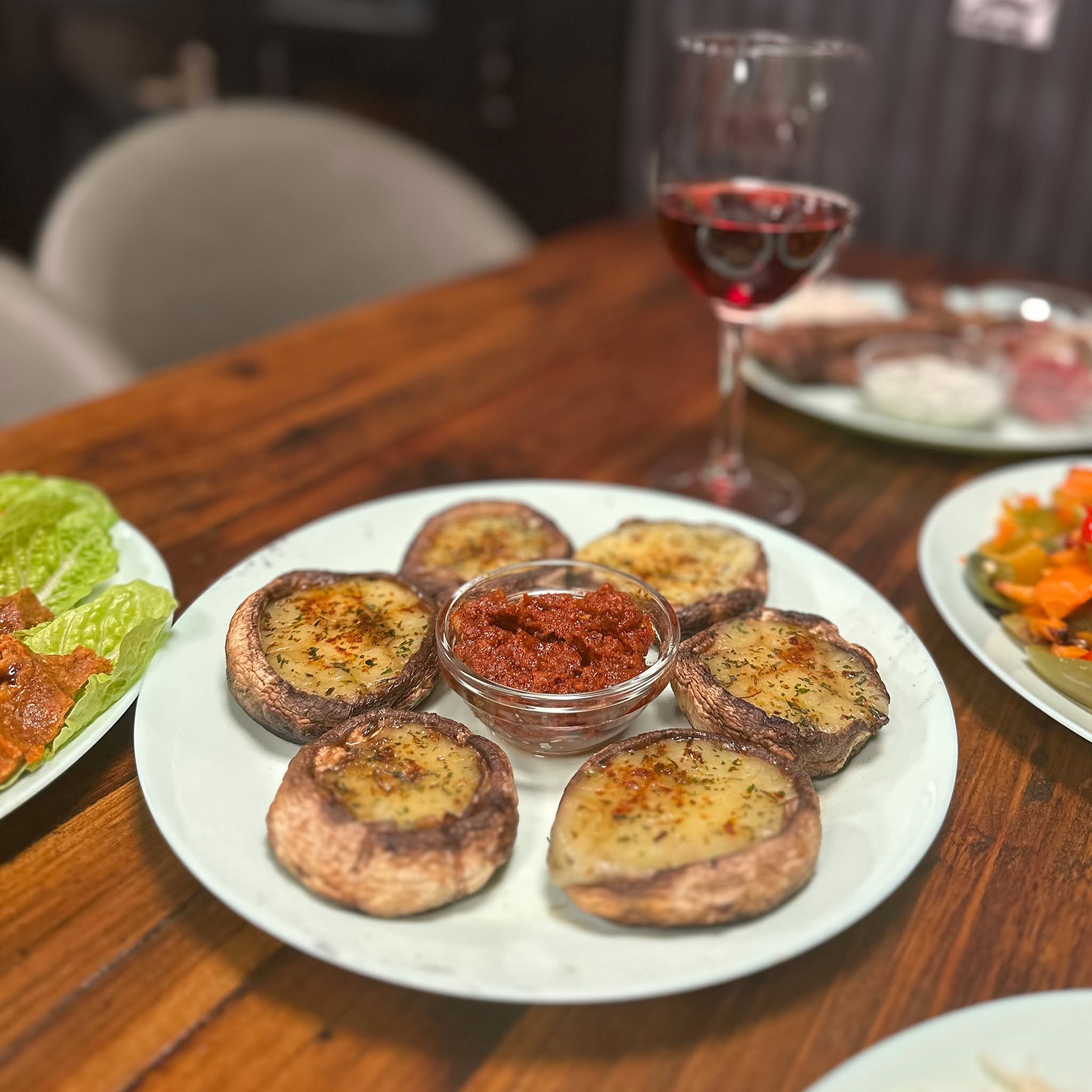 Roasted mushrooms on a white plate with a bowl of red dip
