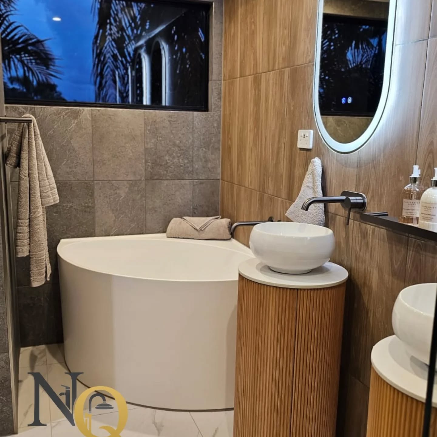 Warm bathroom with stone-look wall tiles, timber fluted vanity and freestanding tub