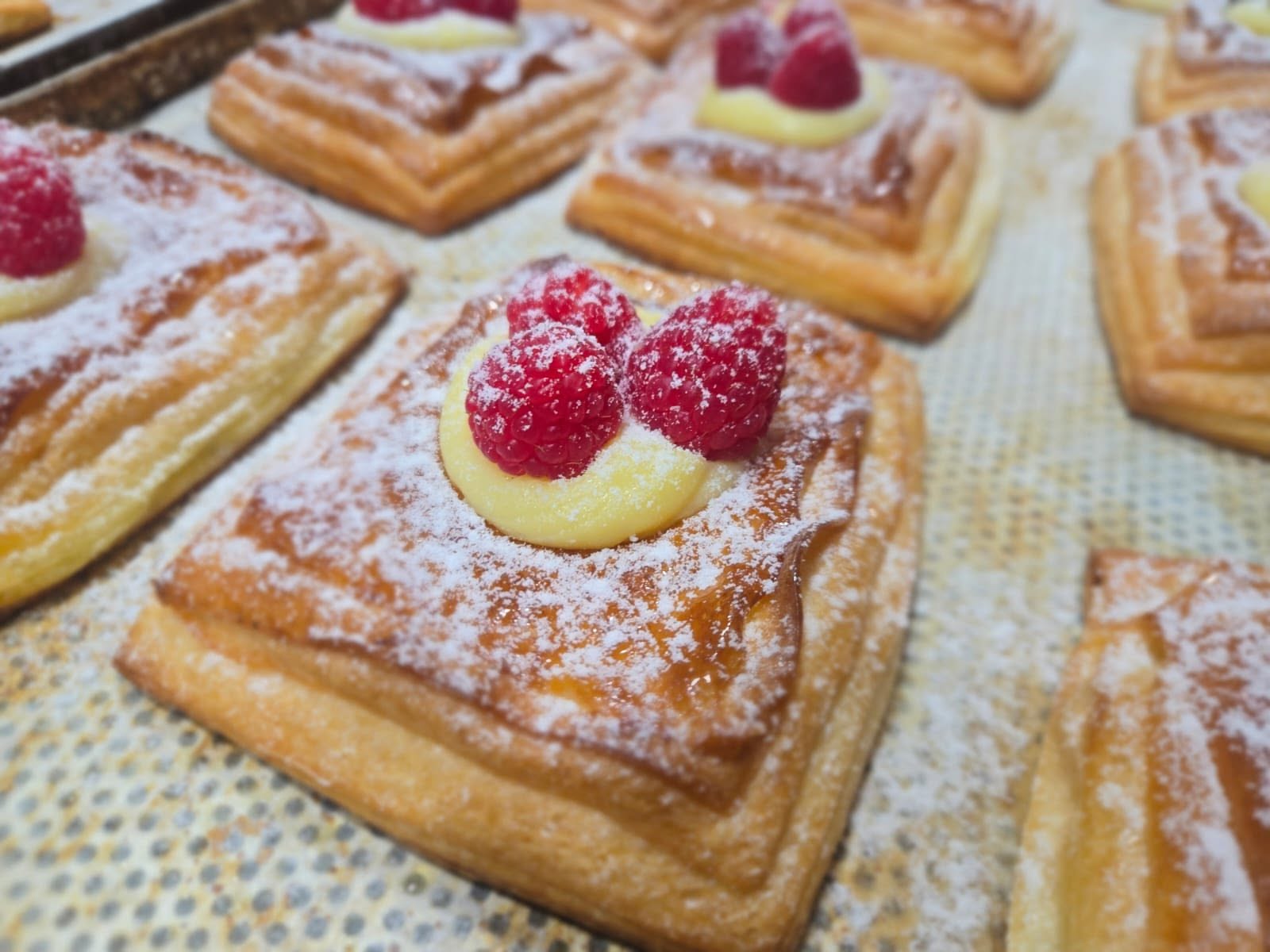 Raspberry Danish pastries dusted with icing sugar on a baking tray
