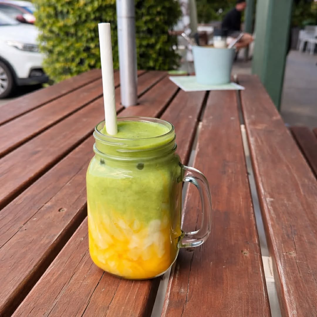 Colourful layered fruit smoothie in a mason jar on a timber outdoor table at Harvest Cafe