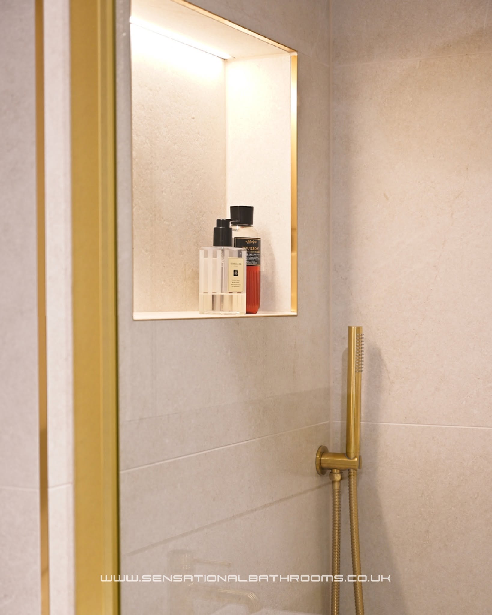 Illuminated shower niche with gold trim and a brushed gold hand shower against stone tiles