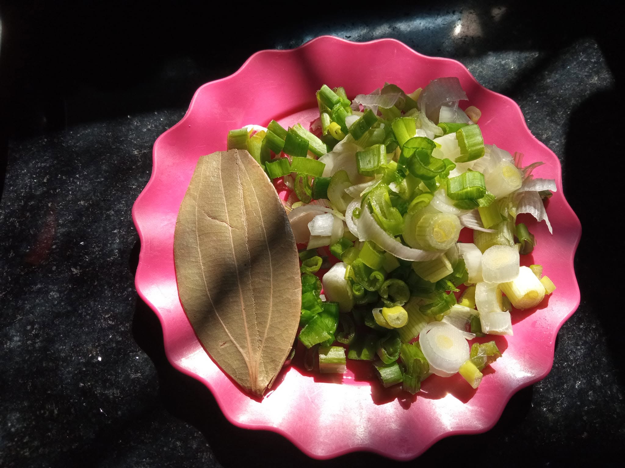 Pink plate with freshly sliced spring onions and bay leaf