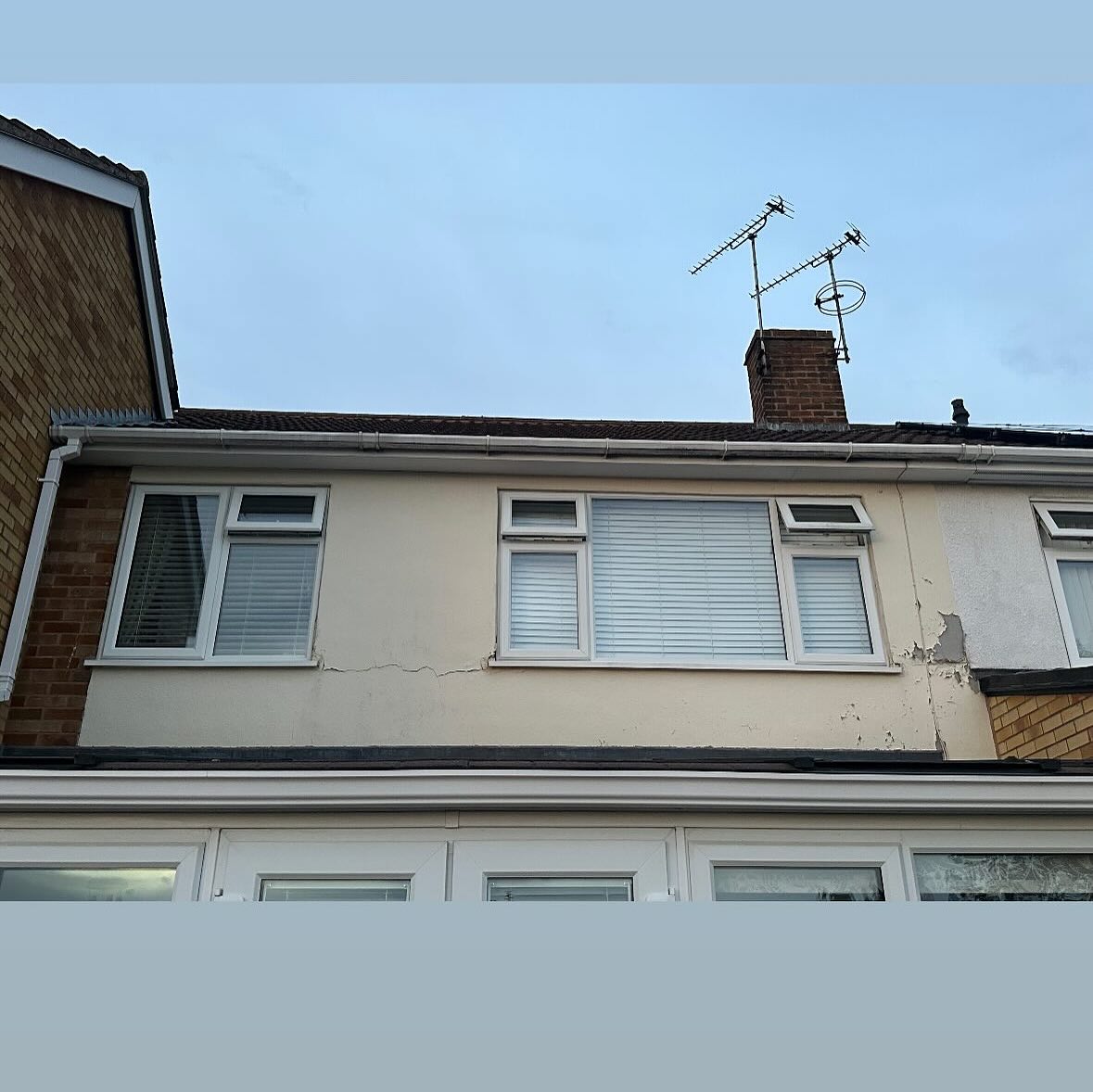 Upper storey of a house with cream render, white window frames and a visible crack in the render