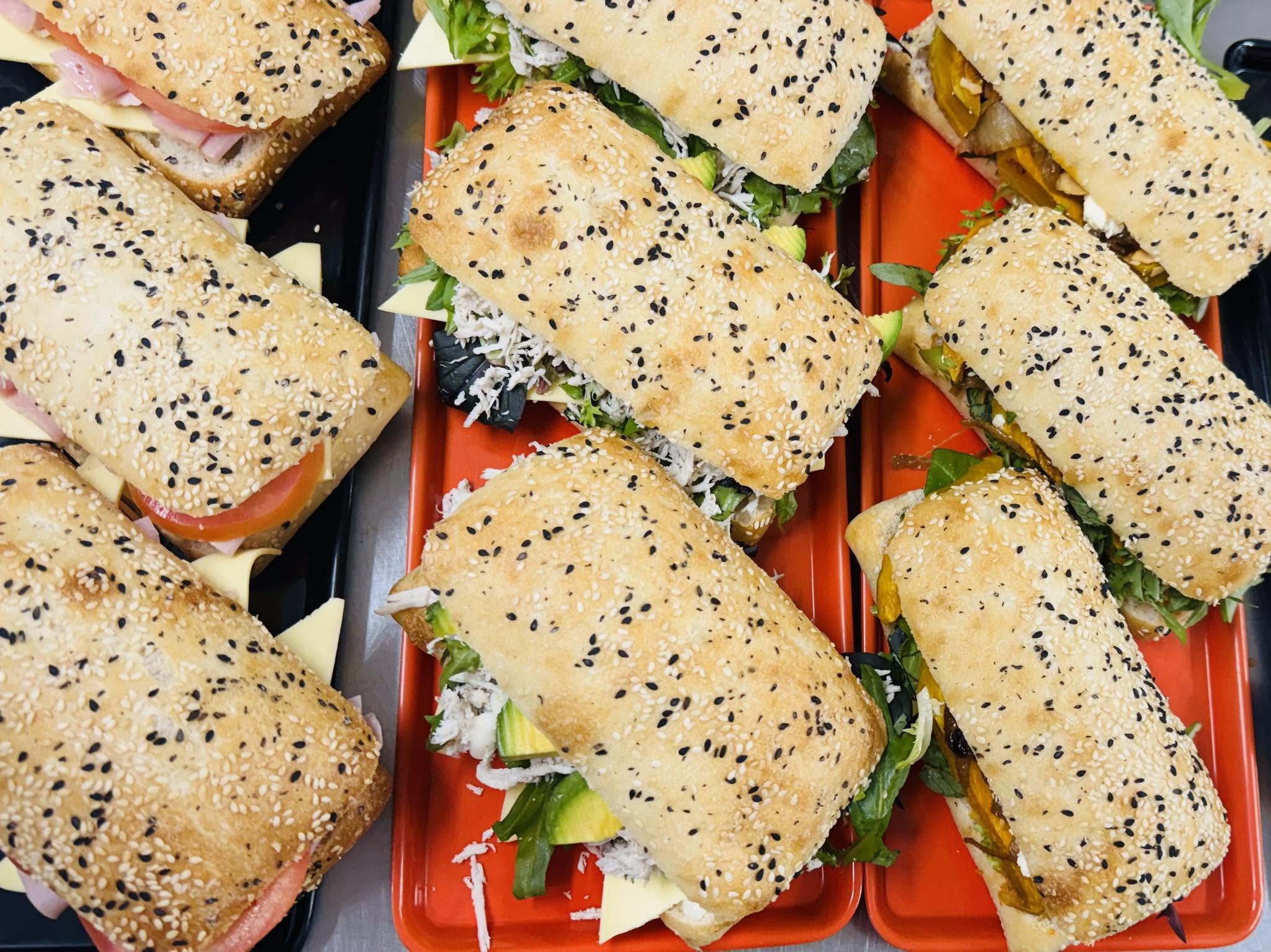 Sesame-topped sandwiches with salad, cheese and tomato on red trays