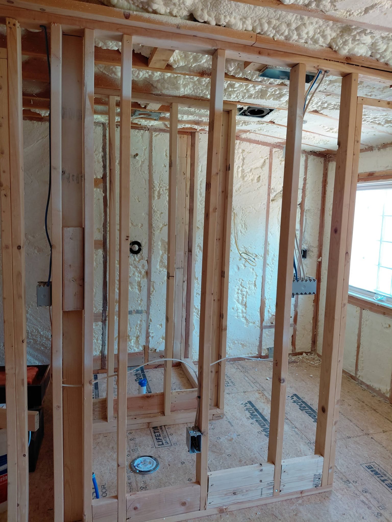 Framing with blue electrical cables, wiring boxes and spray foam insulation