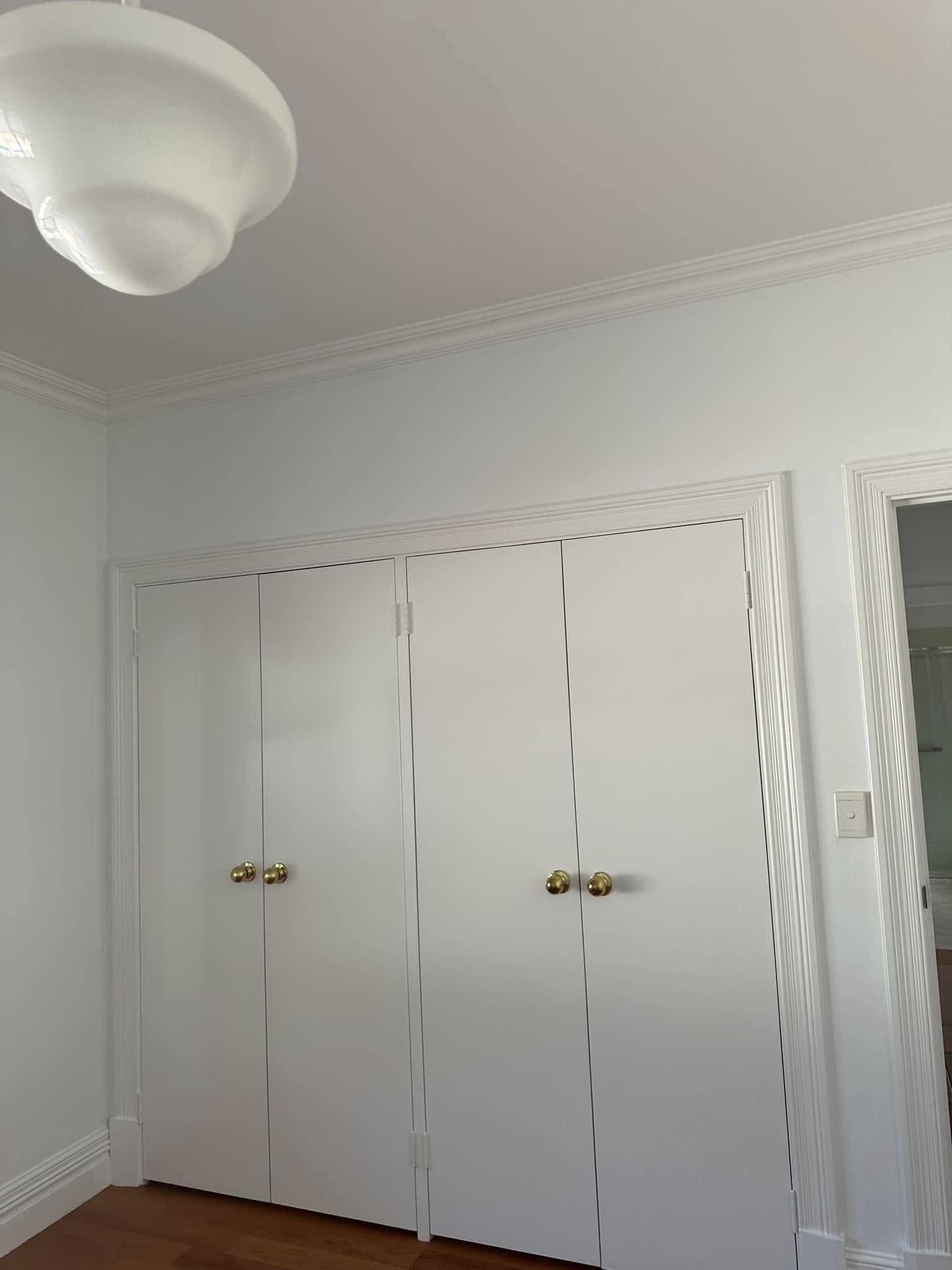 Bright white built-in wardrobes with brass knobs and ornate cornice — property repaint result