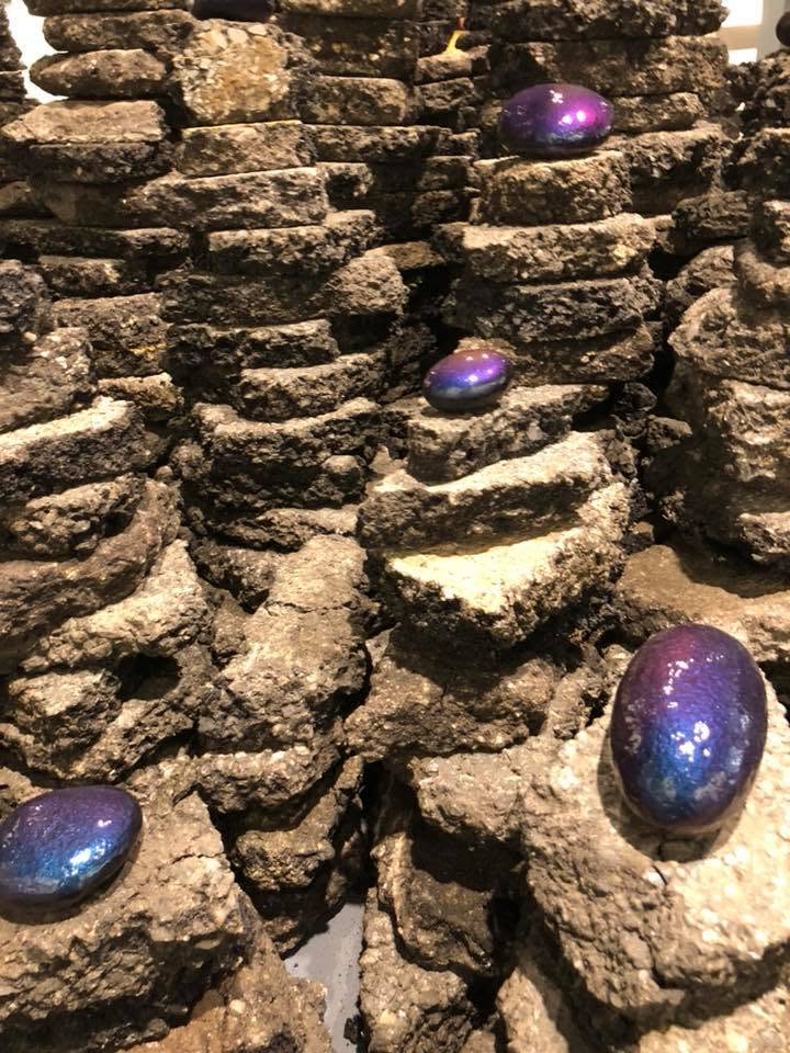 Iridescent purple painted stones nestled in rough coastal rockwork — artwork detail