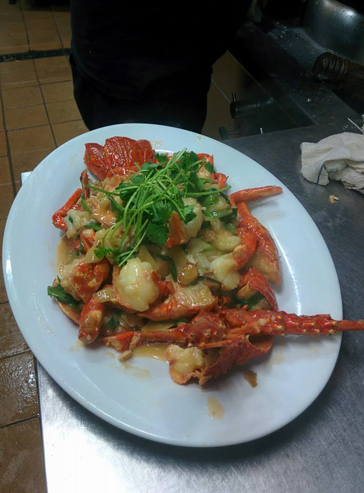 Stir-fried lobster with ginger sauce garnished with fresh coriander on a white plate