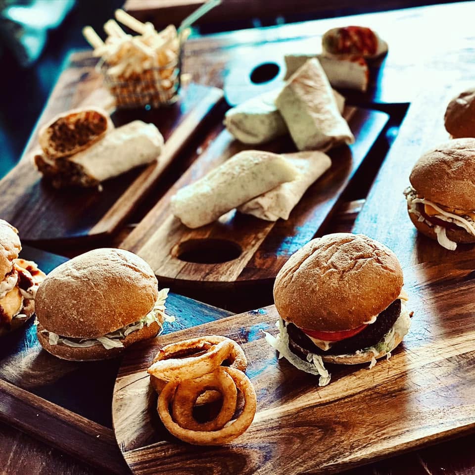 A wooden board loaded with burgers, wraps, onion rings and fries