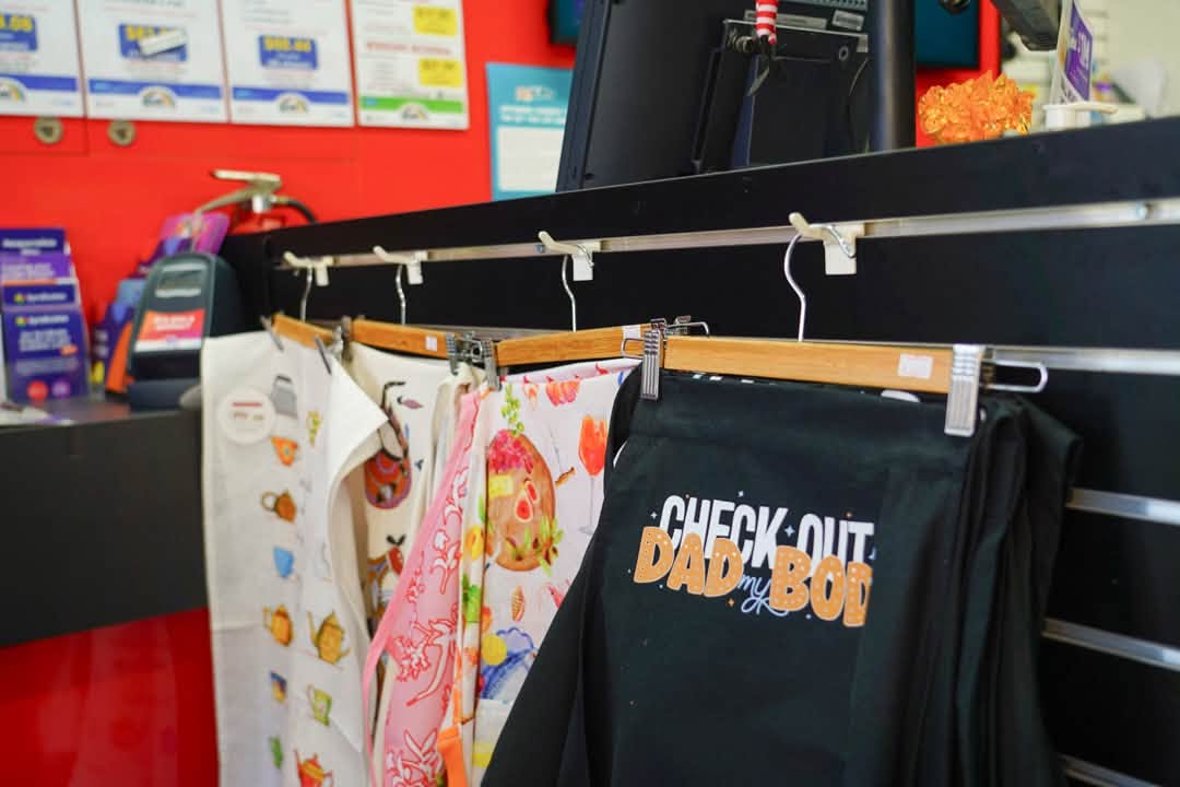 Shop counter with lottery posters on a red wall and aprons on a hanging rail