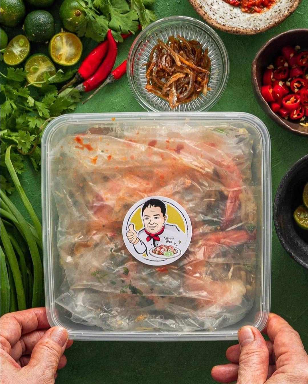 Sealed Hokkien Mee takeaway container with Dennis Wee branding, surrounded by fresh ingredients