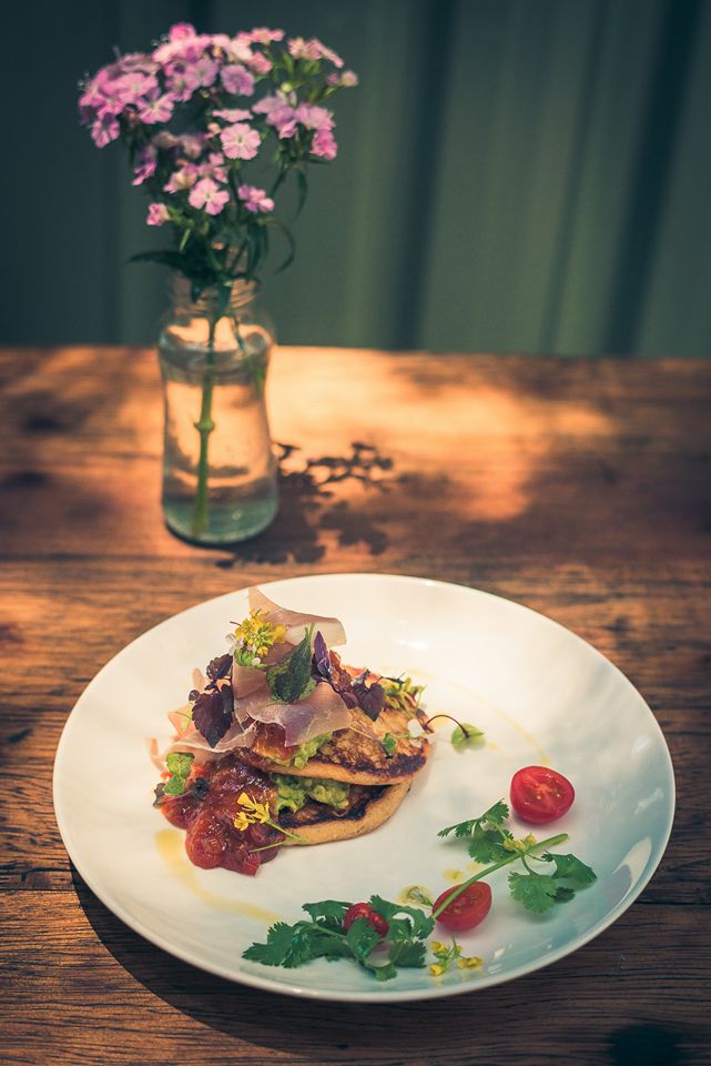 Plated brunch dish with herbs and edible flowers on a timber table at Monday Morning Cafe courtyard