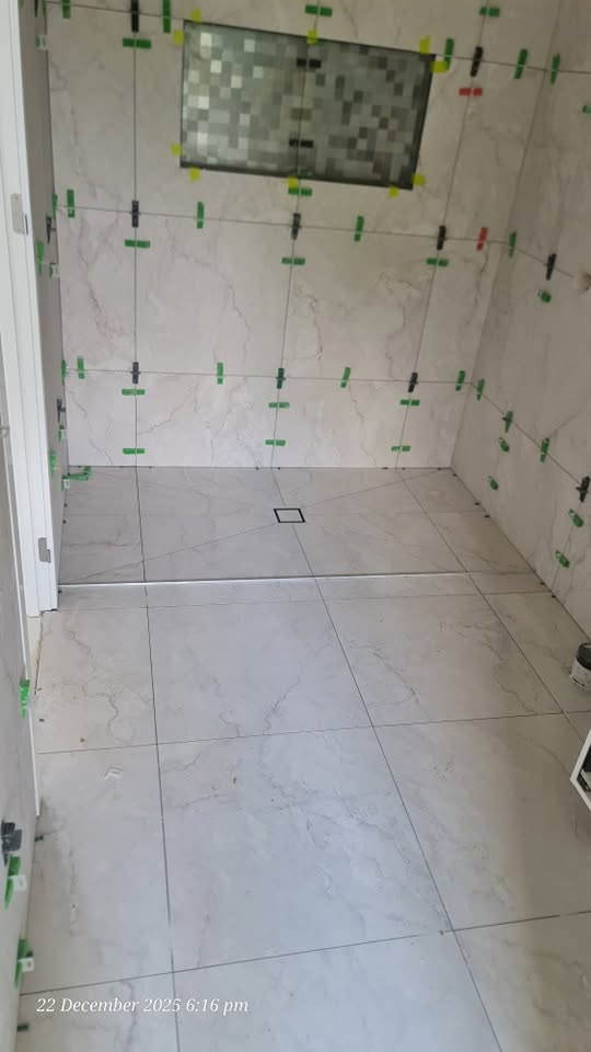 Marble-look bathroom wall and floor tiling in progress with leveling clips