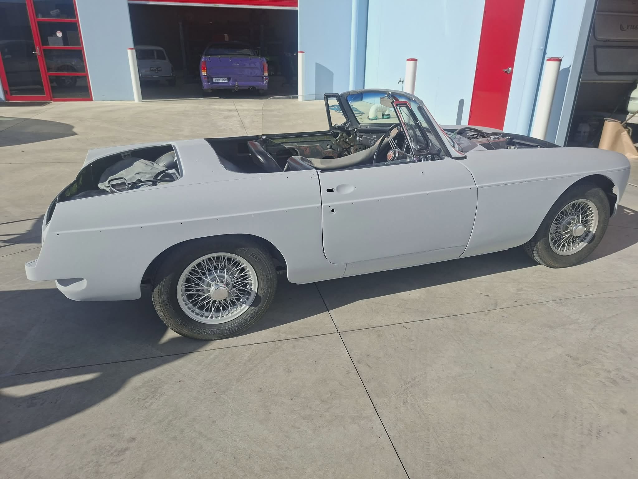 Classic MGB roadster in grey primer, side profile with wire wheels — mid-restoration at April Motors
