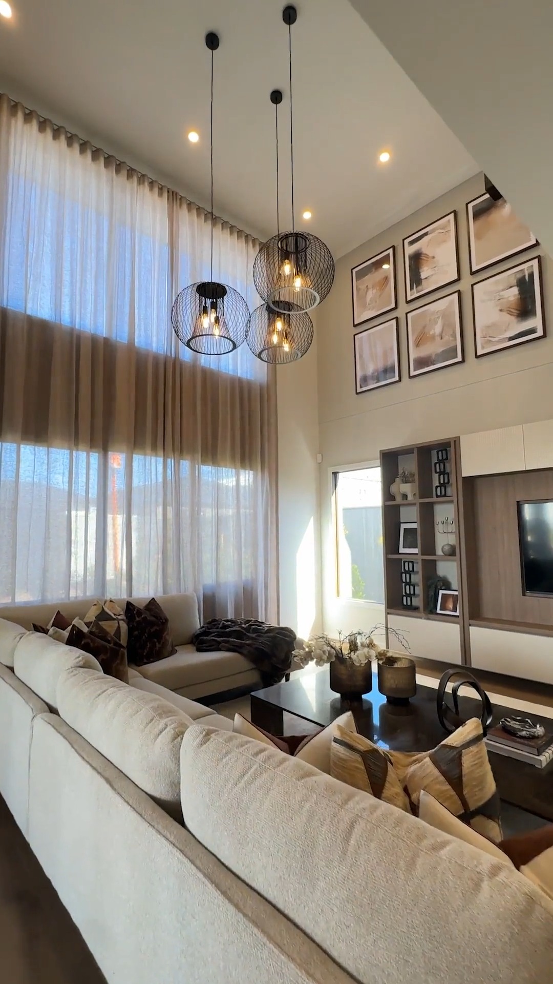 Double-height living room with sheer curtains and statement pendant lighting