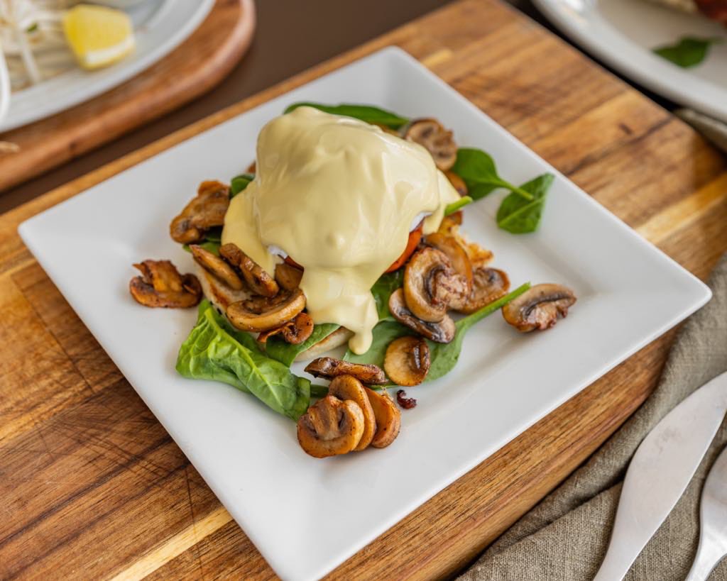 Eggs benedict with sautéed mushrooms, spinach and hollandaise sauce on a wooden board