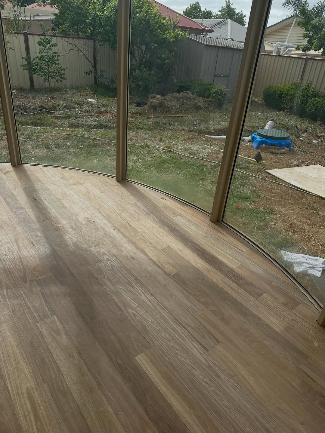 Wide-plank Australian hardwood timber flooring next to curved floor-to-ceiling windows in a new build