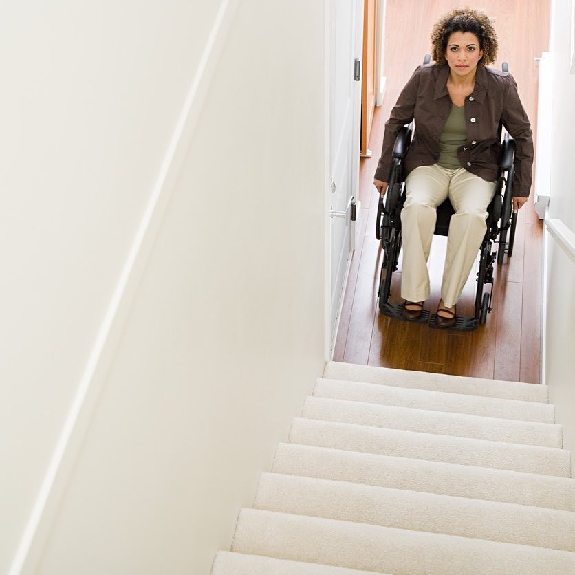 Woman using a wheelchair at the base of a staircase highlighting home accessibility barriers