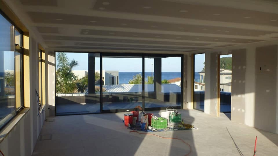 Plastering in progress — large open-plan room with plasterboard ceiling and ocean view through windows