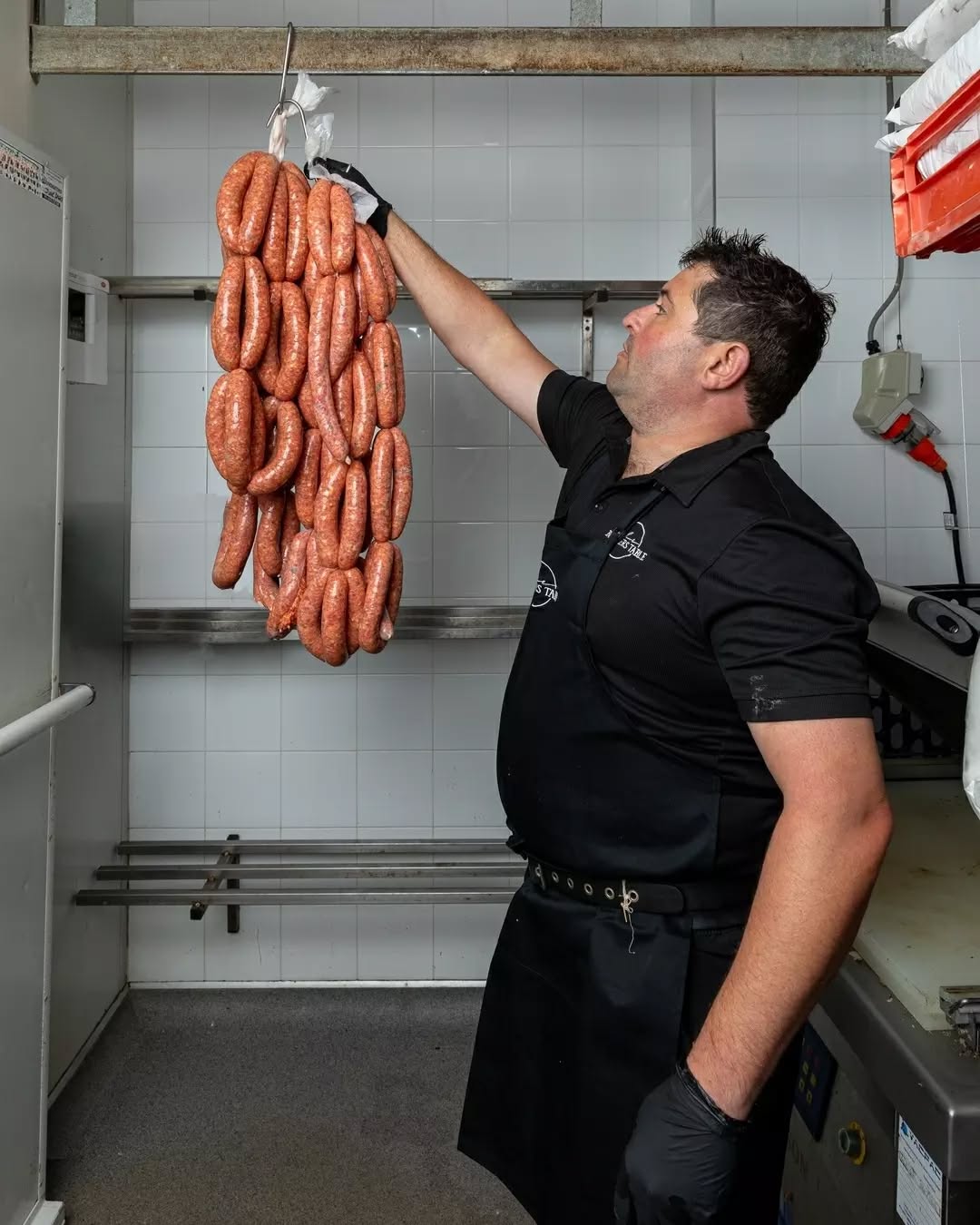 Butcher reaching up to hang fresh sausage links on a rack