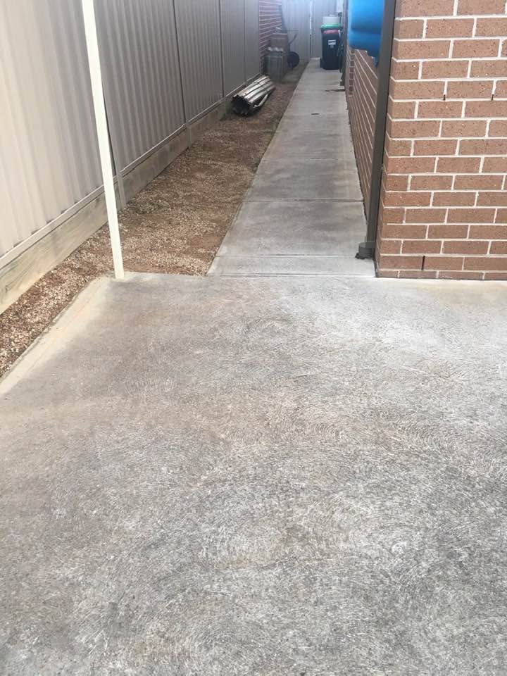 Clean concrete pathway beside a brick home after pressure cleaning