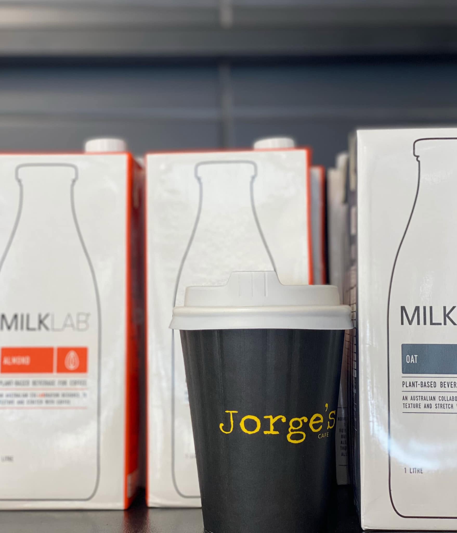 Jorge's Cafe branded takeaway cup alongside plant-based milk cartons