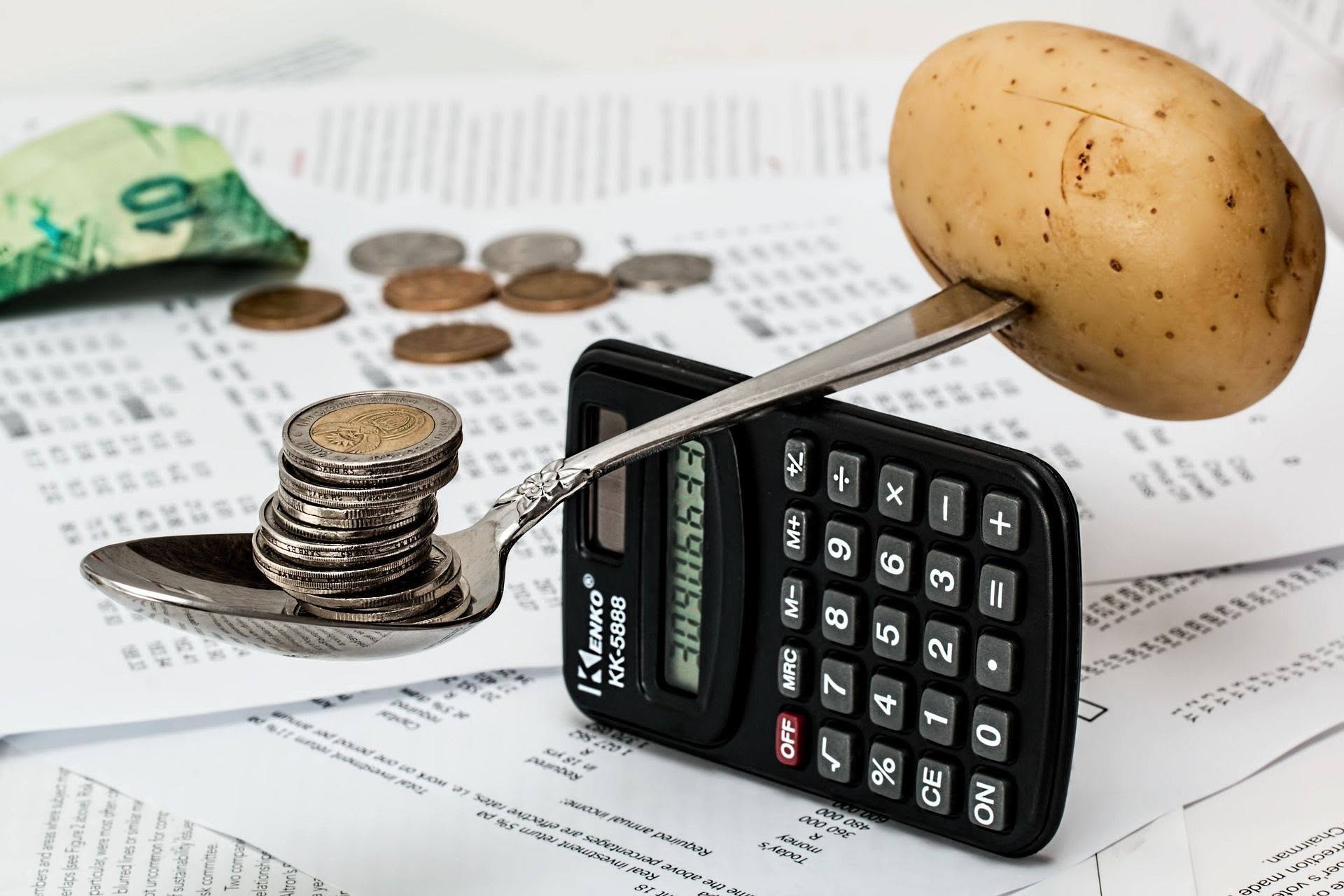 Coins balanced on a spoon opposite a calculator, set on printed financial papers