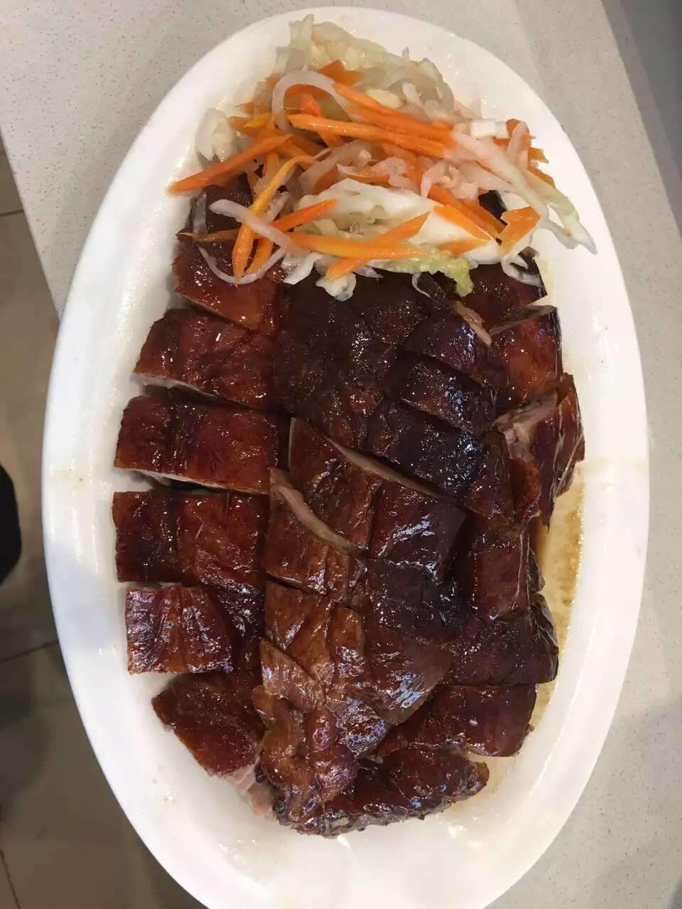 Sliced BBQ roasted pork belly on a white plate with pickled vegetables