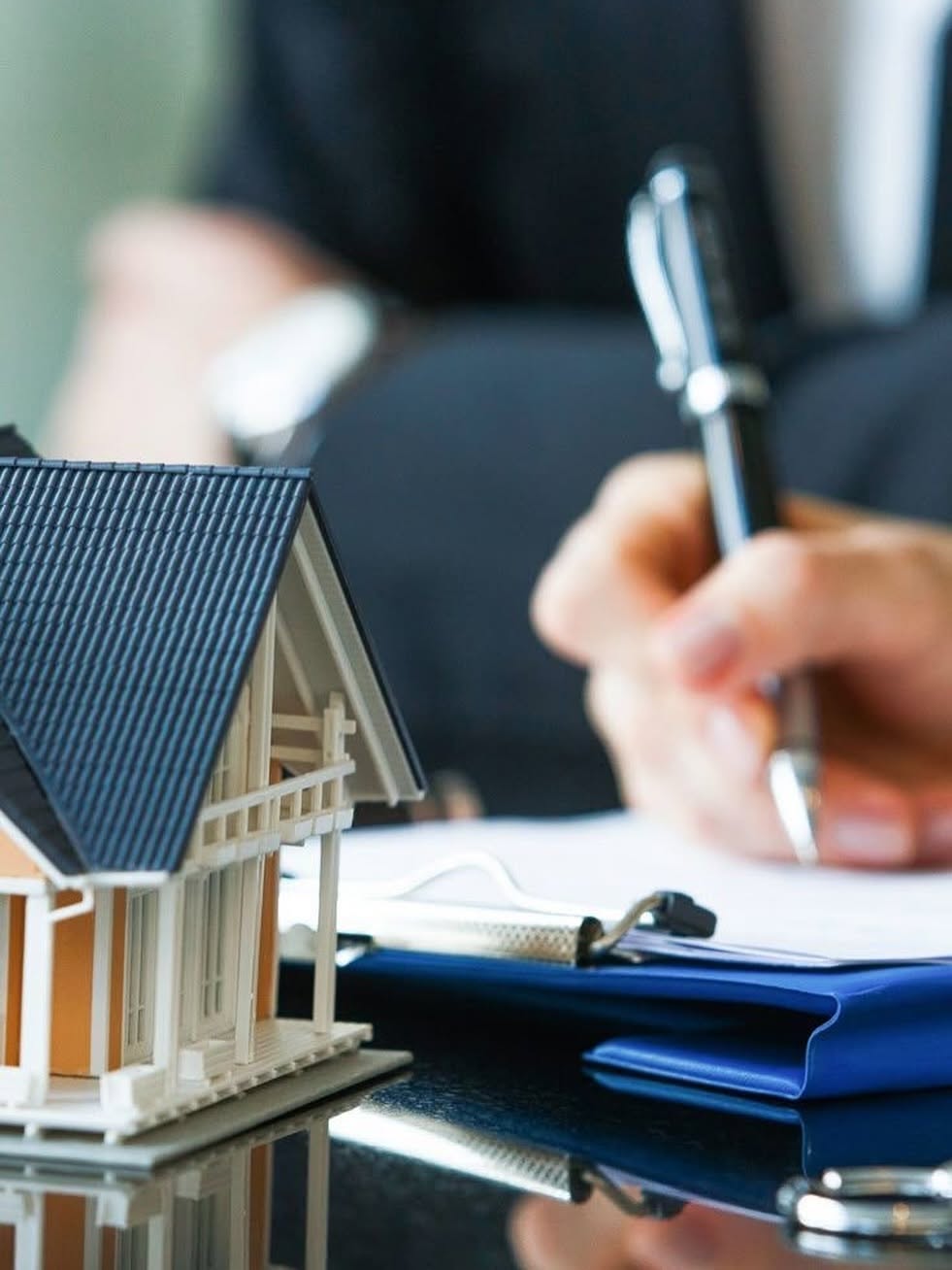 Financial adviser writing on clipboard with house model, representing retirement and asset planning
