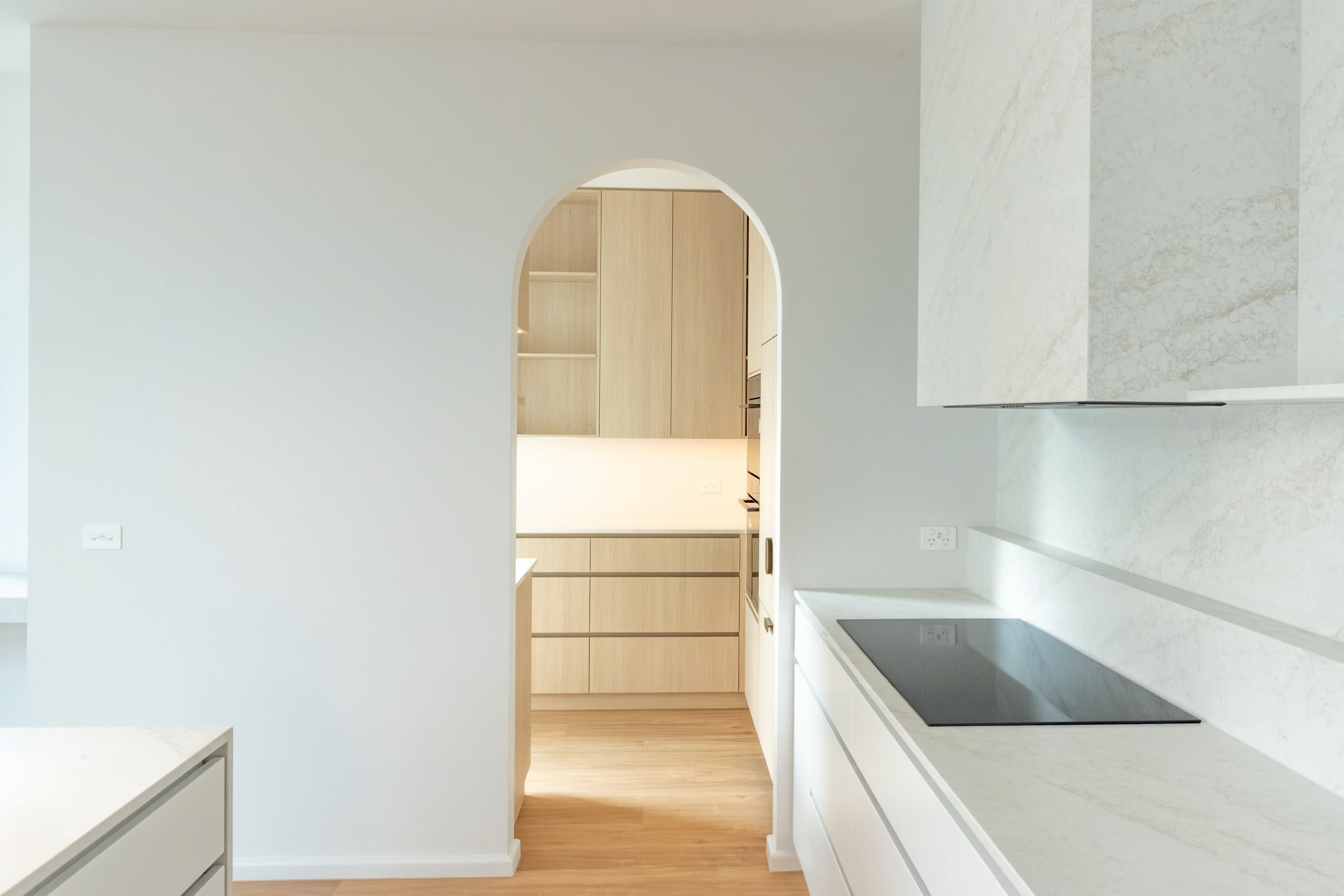 A bright, custom-built kitchen with timber cabinetry visible through an arched doorway