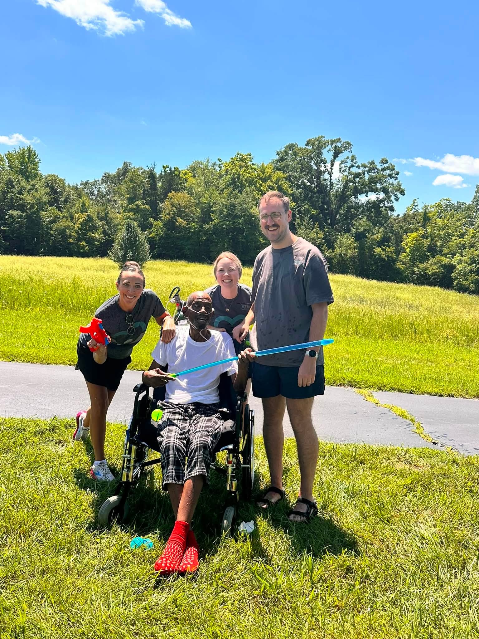 Ahava therapy team members with a resident in a wheelchair outdoors in a green field