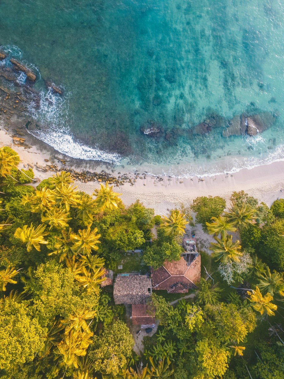 Letecký pohled na pláž, tyrkysové moře a domek obklopený palmami na Srí Lance