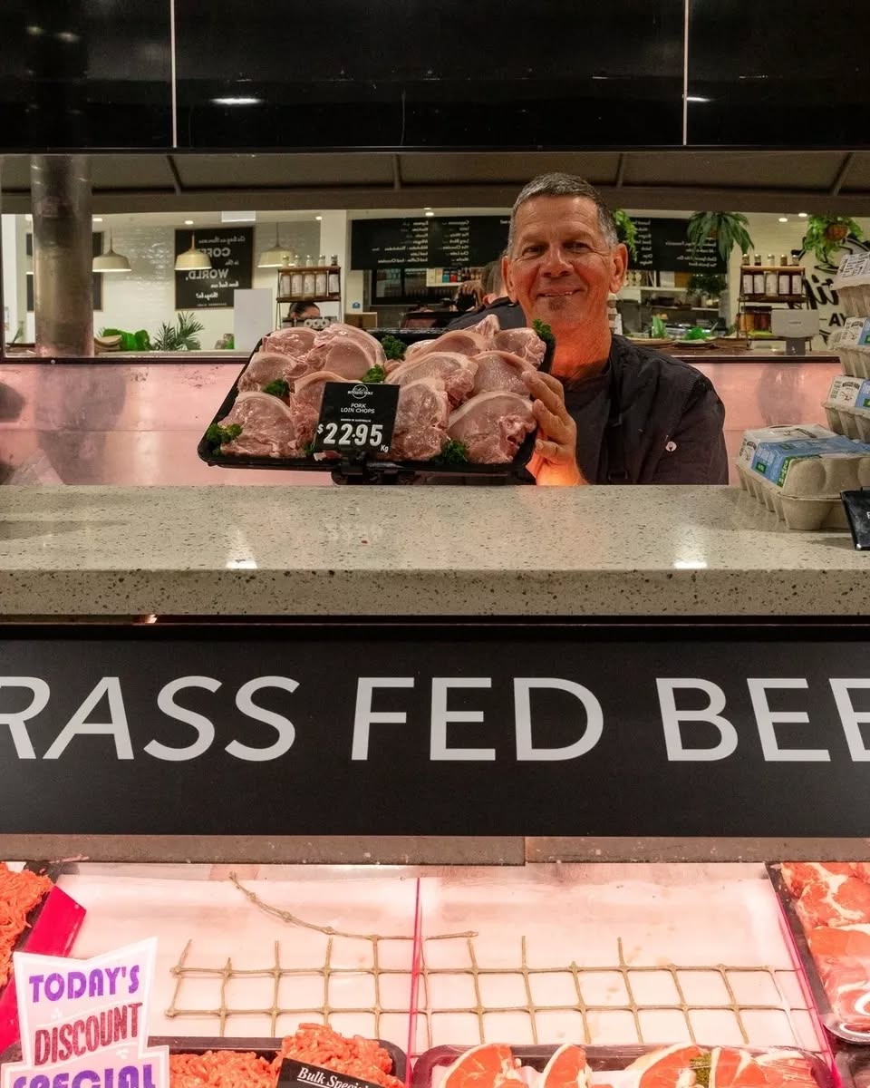 Butcher behind the counter proudly presenting pork loin chops above a grass-fed beef sign