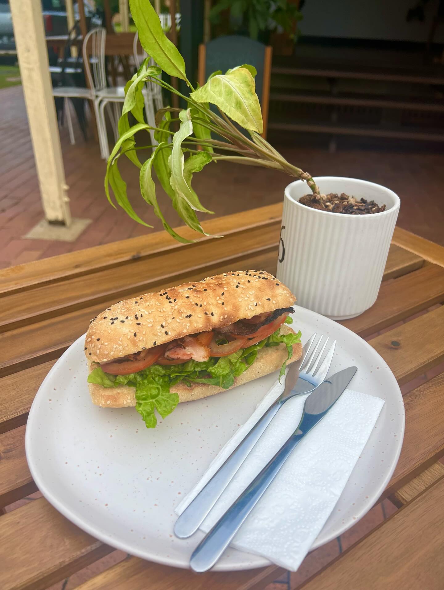 Freshly made sesame-seed baguette roll with bacon, lettuce and tomato on a white speckled plate at Hygge Cafe
