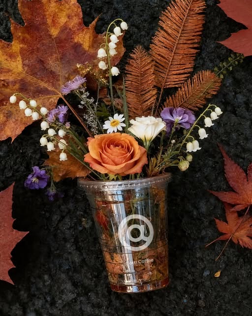 A clear Cotti Coffee cup used as a vase with autumn flowers — capturing the brand's creative and artistic side