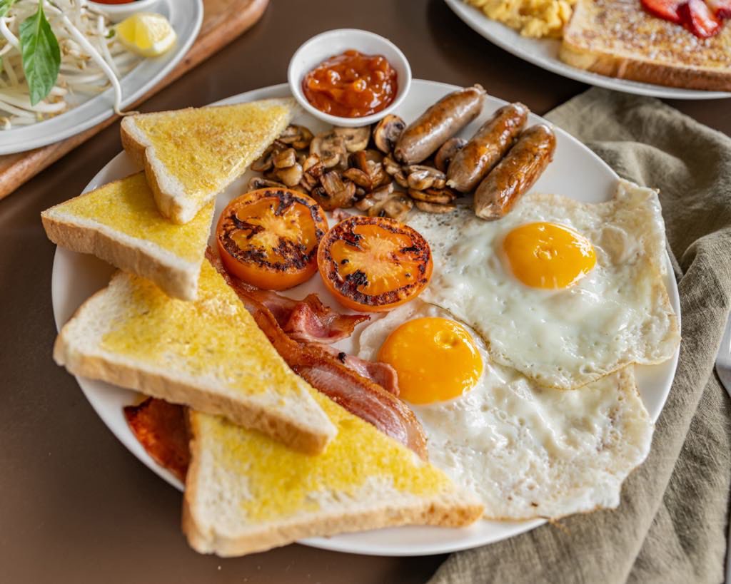 Big breakfast plate with fried eggs, bacon, sausages, grilled tomatoes, mushrooms and buttered toast