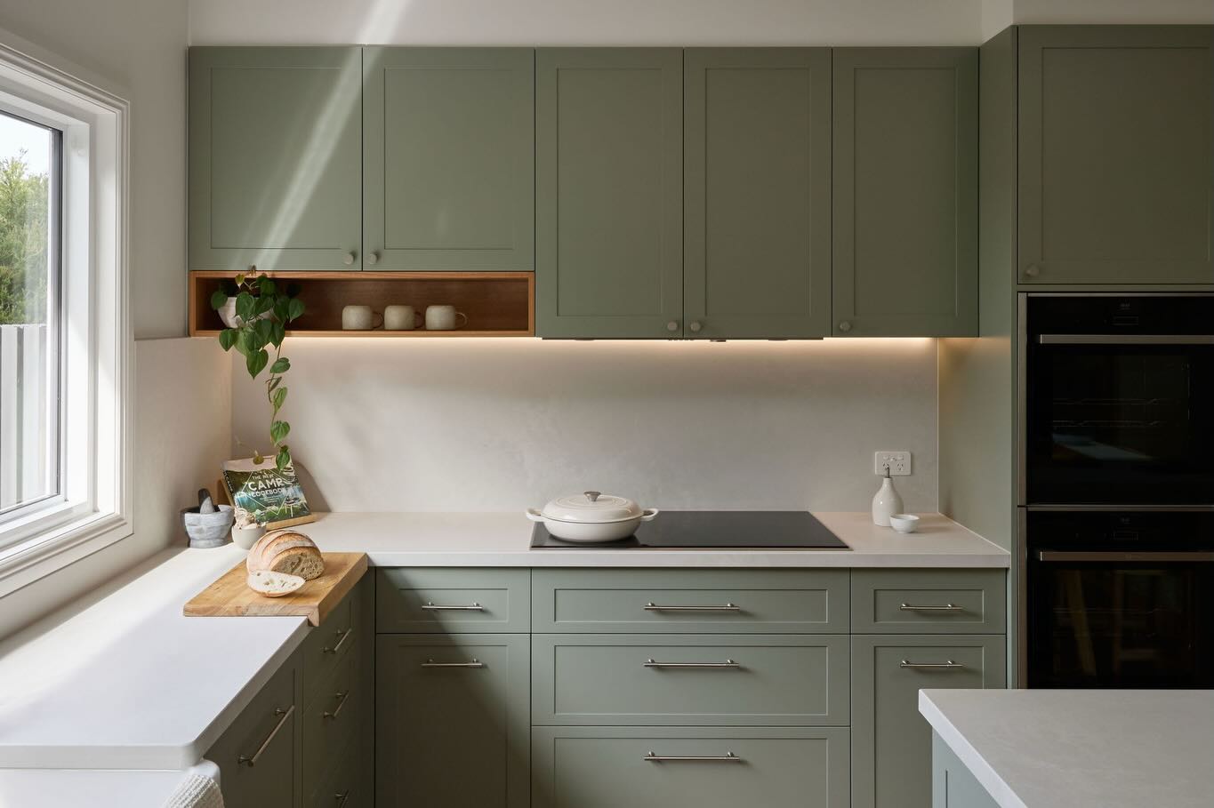 Sage green kitchen cabinetry with timber open shelving and a wooden cutting board
